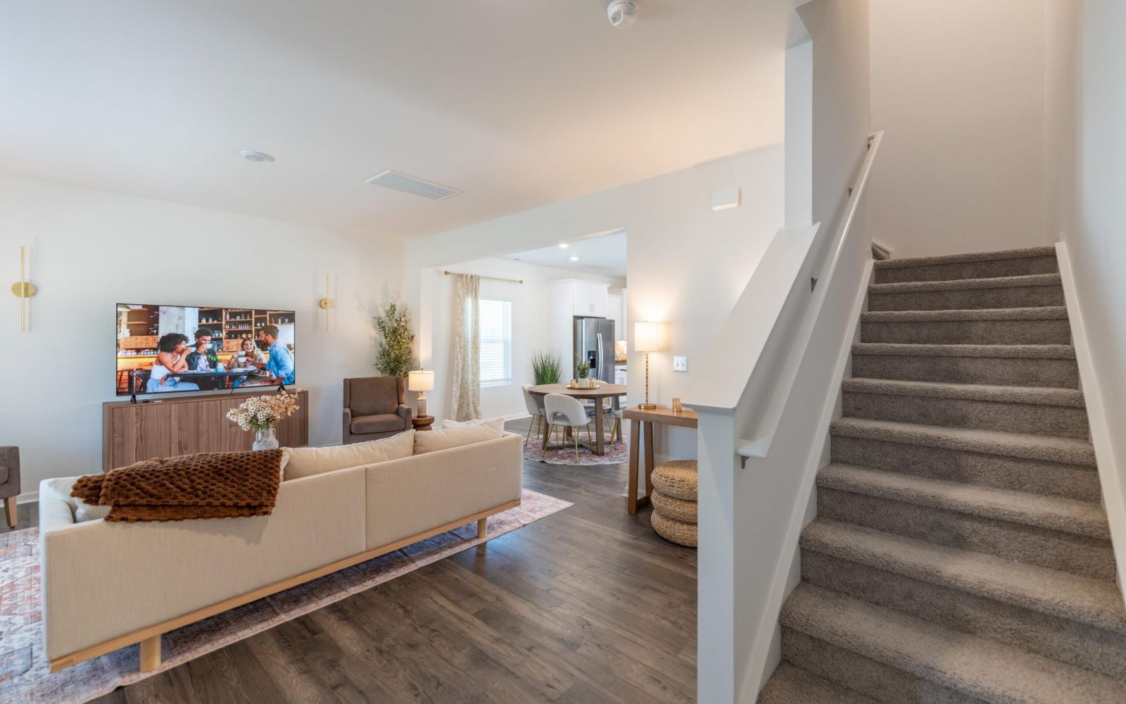 The Bend at Cramerton Mills bright, modern living room with a white sofa, TV, and open view of kitchen and dining area.