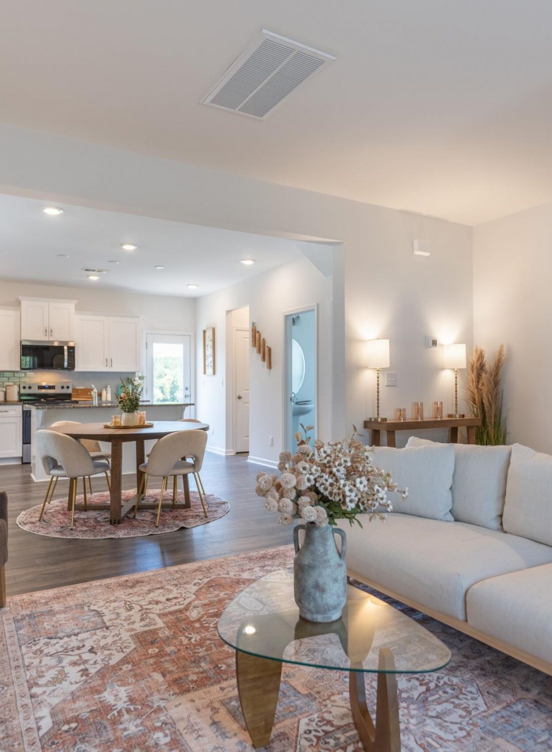The Bend at Cramerton Mills modern open-concept living and dining area with neutral decor, a sofa, glass table, and kitchen in the background.