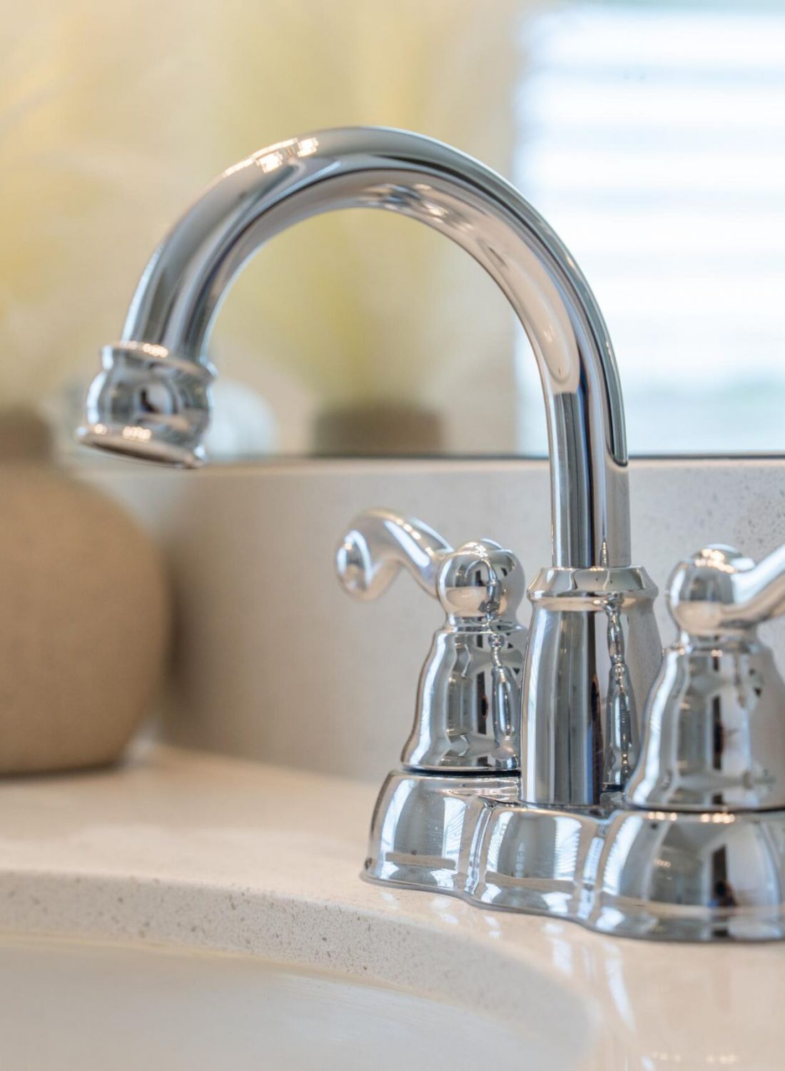 The Bend at Cramerton Mills close-up of a shiny chrome bathroom faucet with two handles on a white sink.