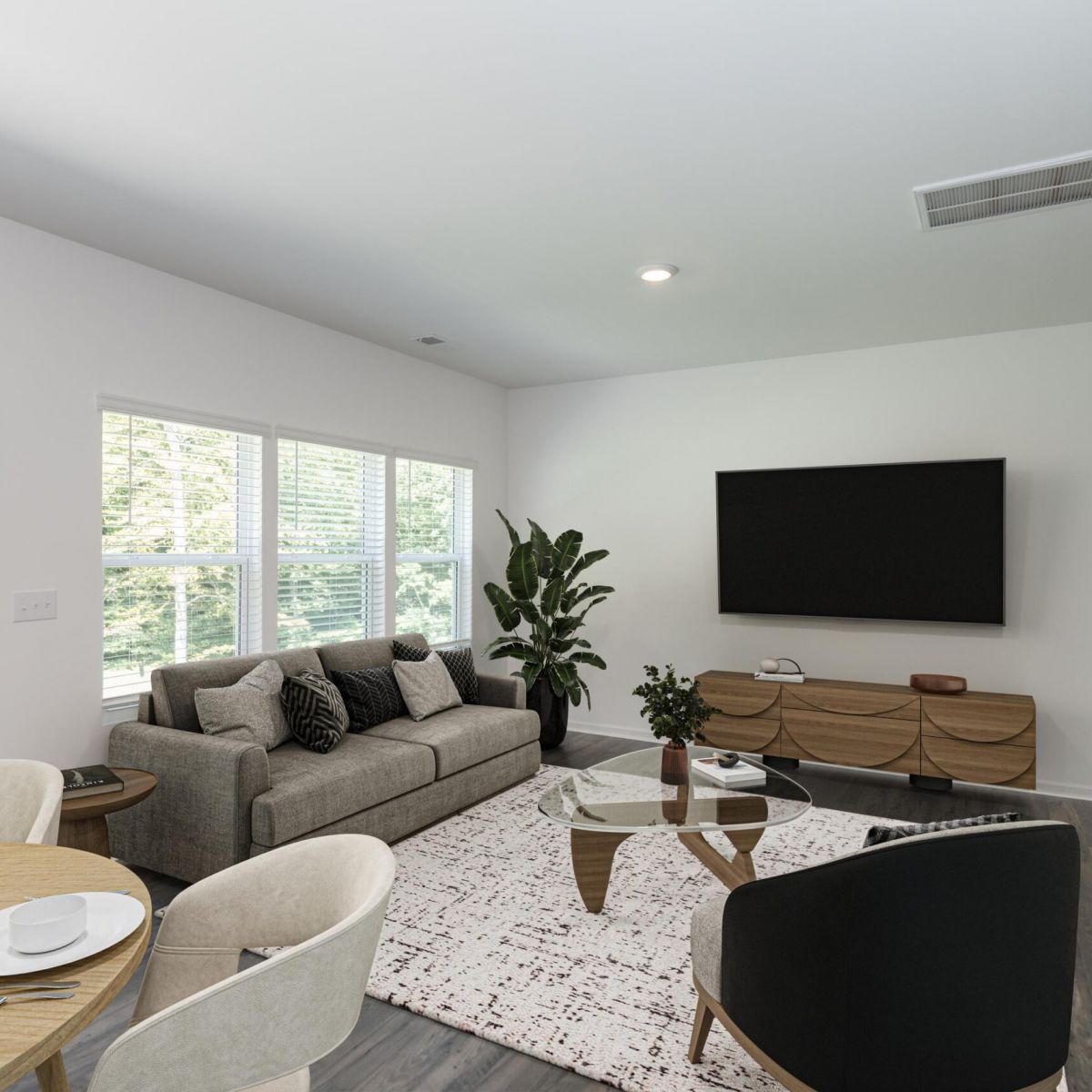 The Bend at Cramerton Mills modern living room with a gray sofa, round coffee table, TV on the wall, and large windows with natural light.