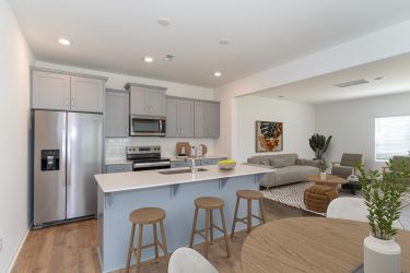 The Bend at Cramerton Mills Modern kitchen with gray cabinets, stainless steel appliances, and a breakfast bar with three wooden stools.