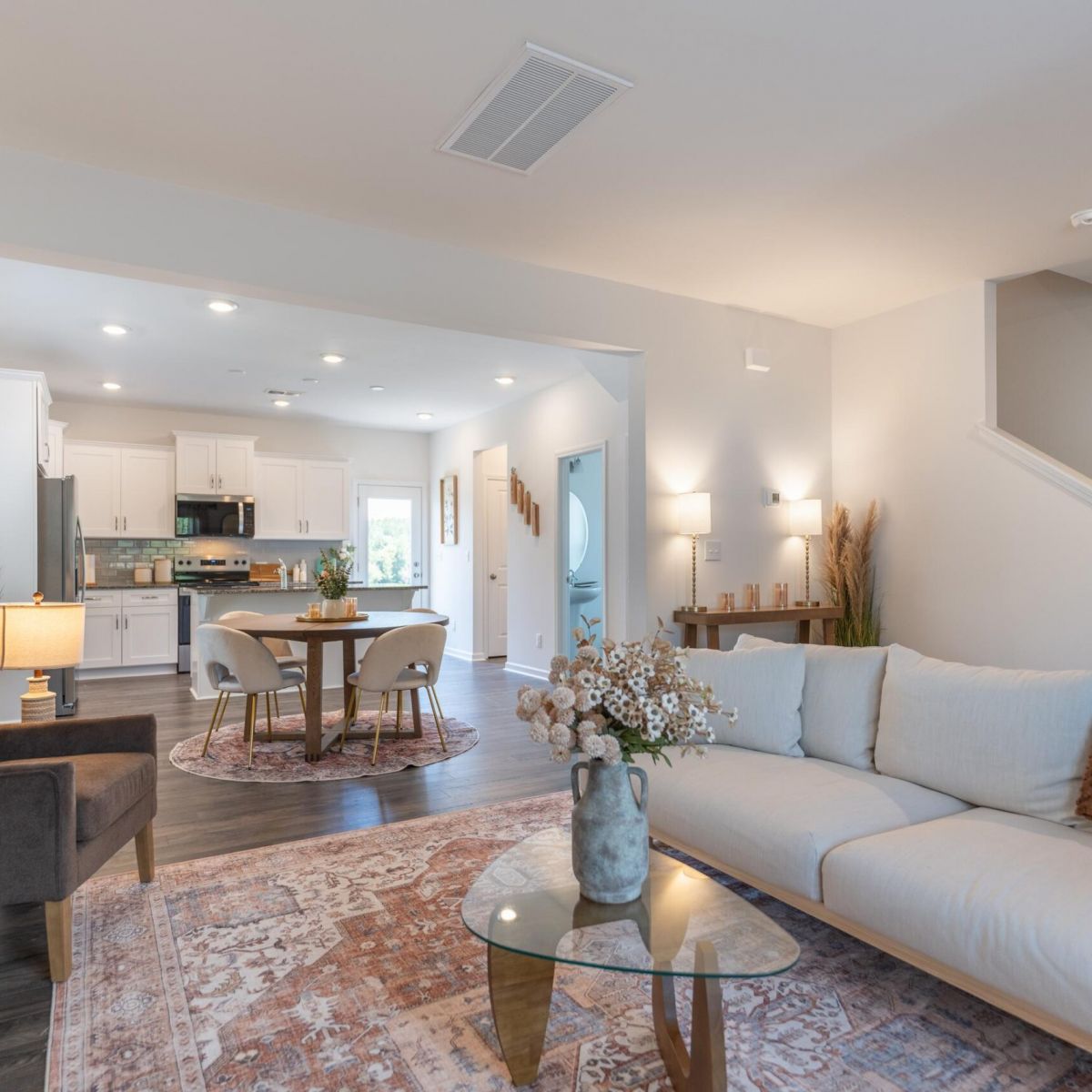 The Bend at Cramerton Mills modern open-concept living and dining area with neutral decor, a sofa, glass table, and kitchen in the background.